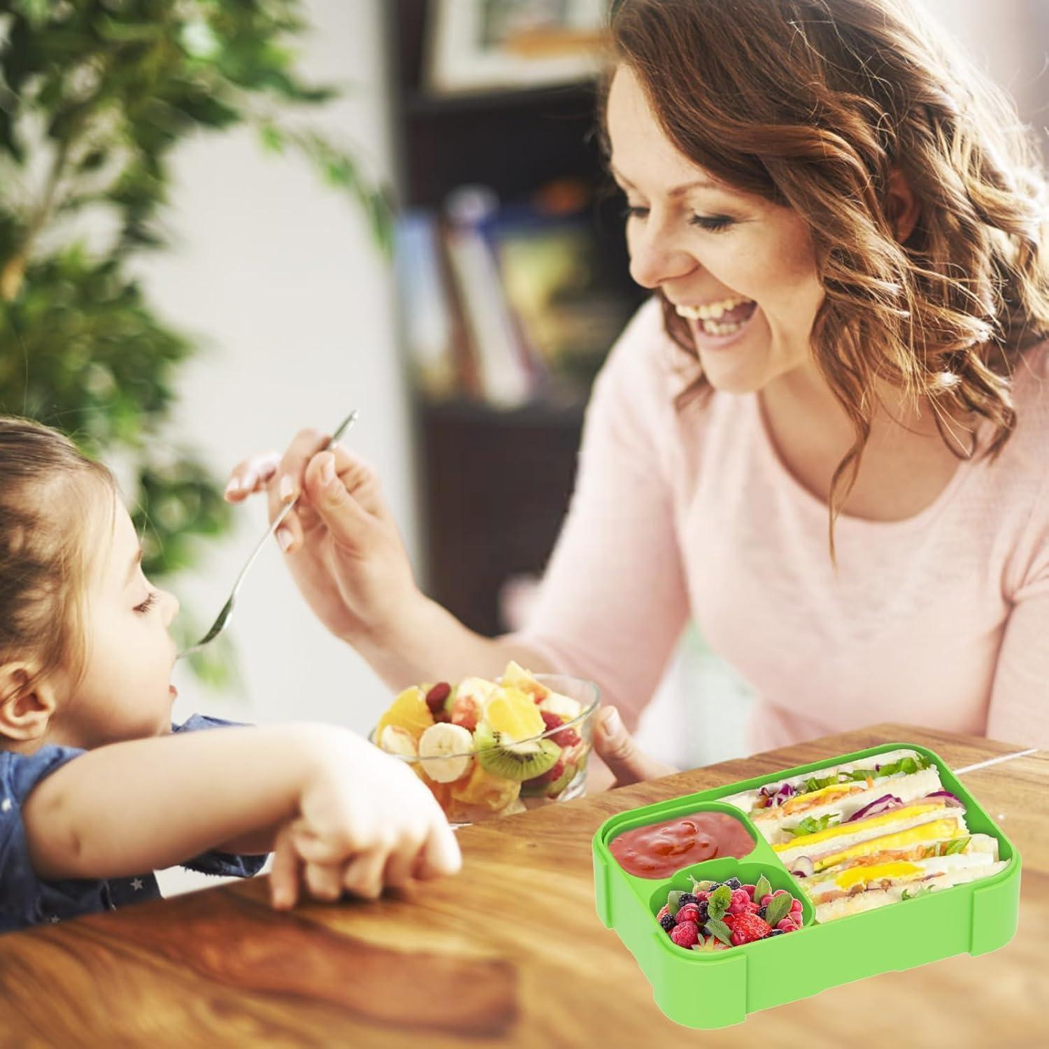 Una madre dà della frutta alla figlia mentre un portapietanze verde con panini è sul tavolo.