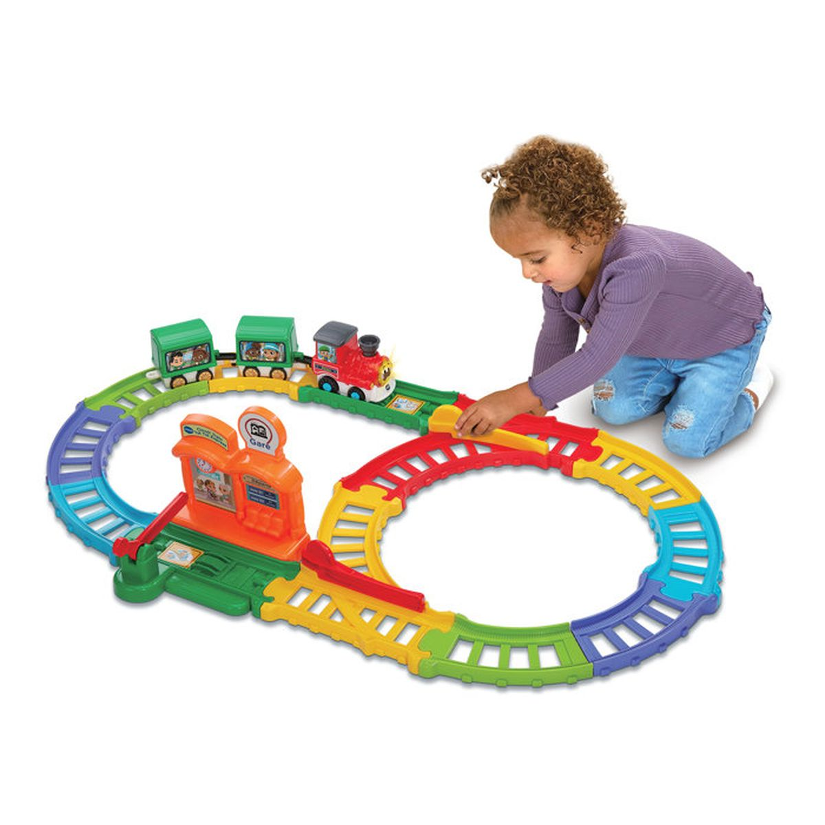 Kleinkind spielt auf dem Boden mit einem bunten Spielzeugeisenbahnset.