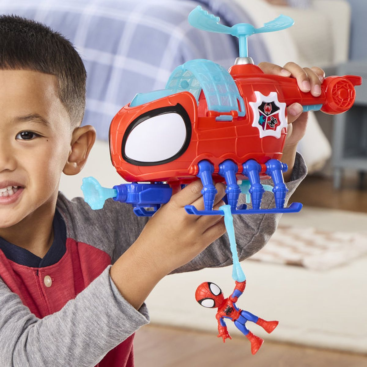 Un garçon souriant tient fièrement un hélicoptère jouet Spider-Man rouge et bleu avec une figurine.