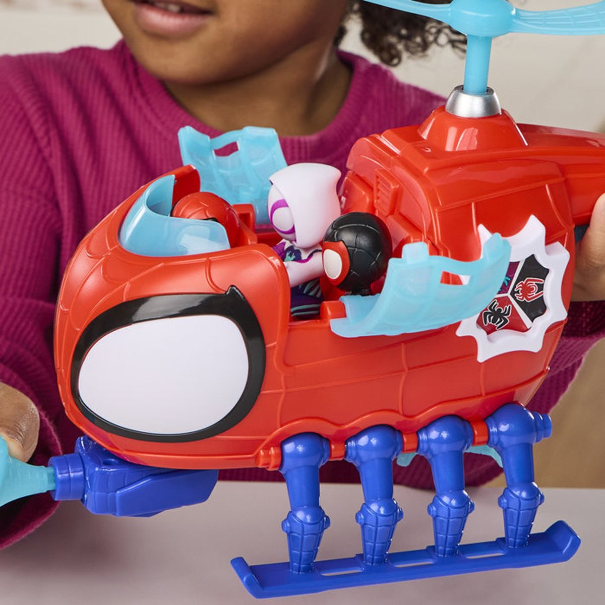 Un enfant tient un hélicoptère jouet rouge avec des pieds bleus et trois figurines dans le cockpit.