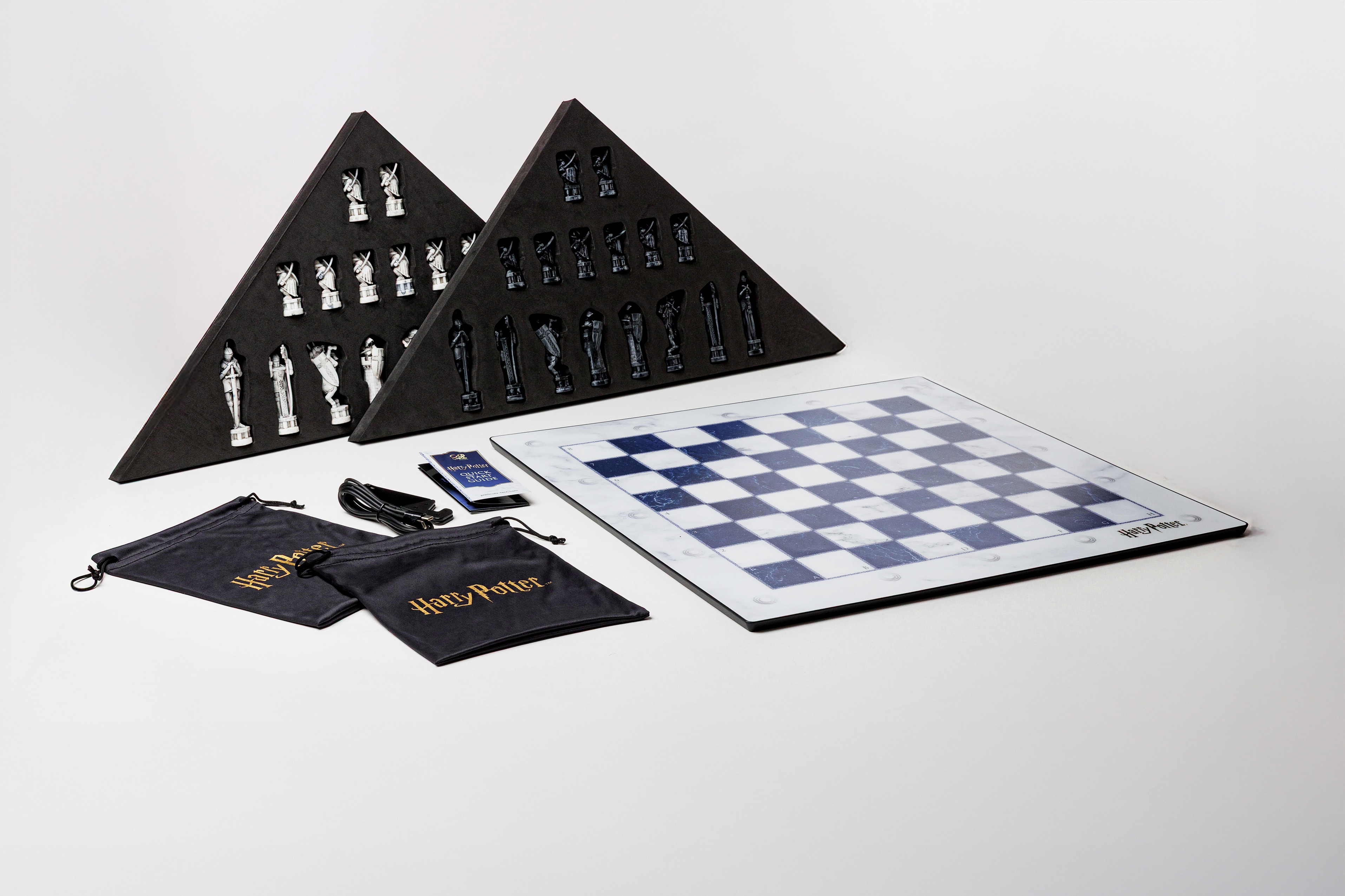 Jeu d'échecs Harry Potter avec plateau bleu et blanc, pièces dans des triangles en mousse et deux sacs en tissu.