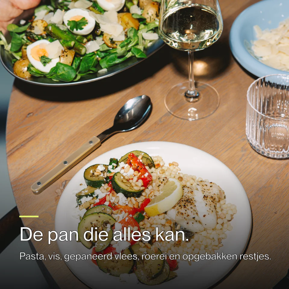A plate of couscous with fish, vegetables, and lemon, next to a glass of white wine and a large salad.