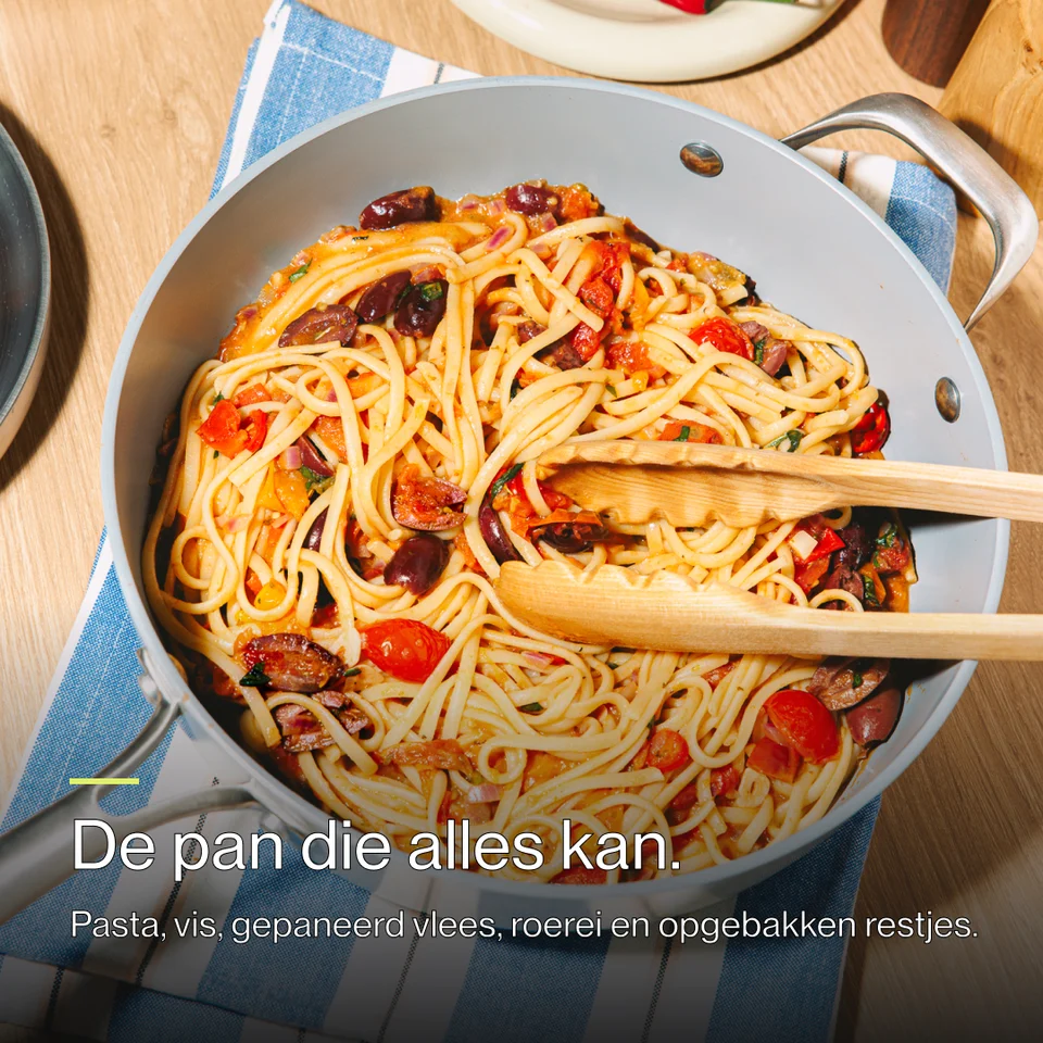 Cooked pasta with tomatoes and olives in a grey pan on a blue striped cloth.