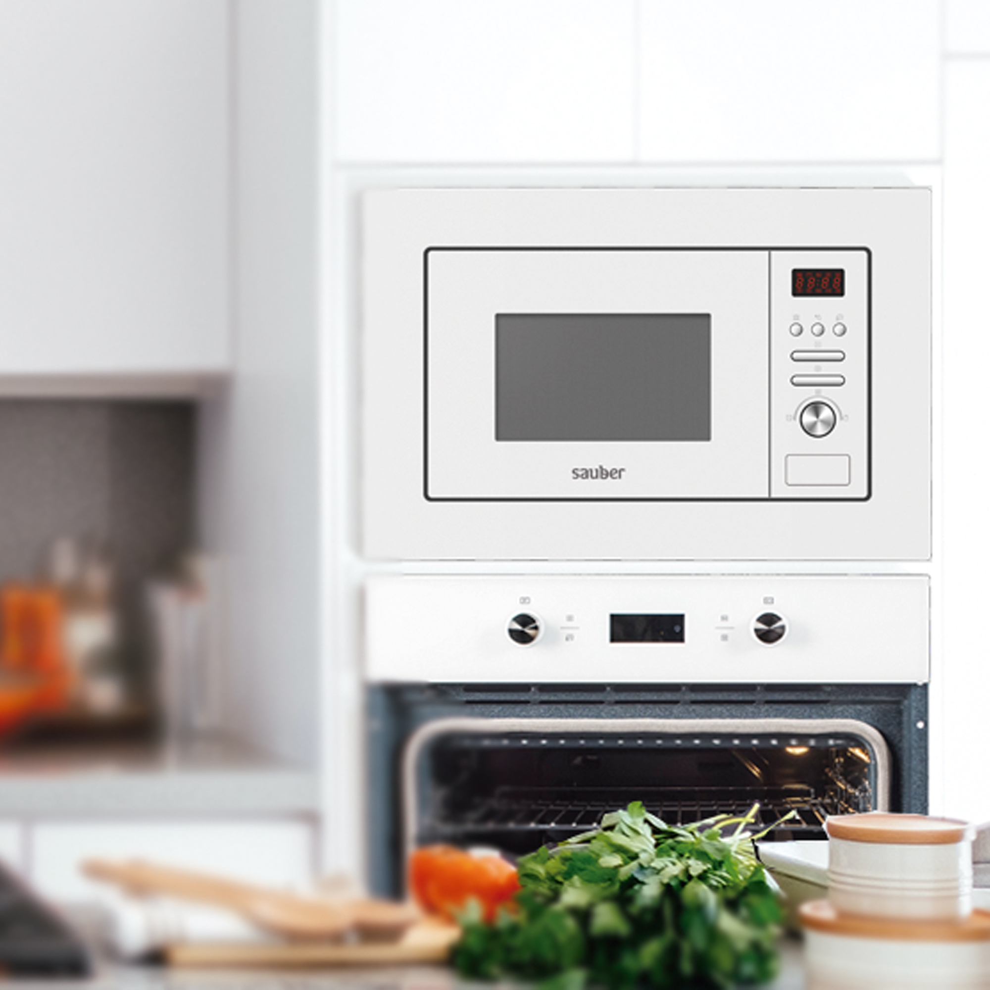 Microondas empotrable blanco sobre un horno abierto con hierbas frescas en el mostrador.