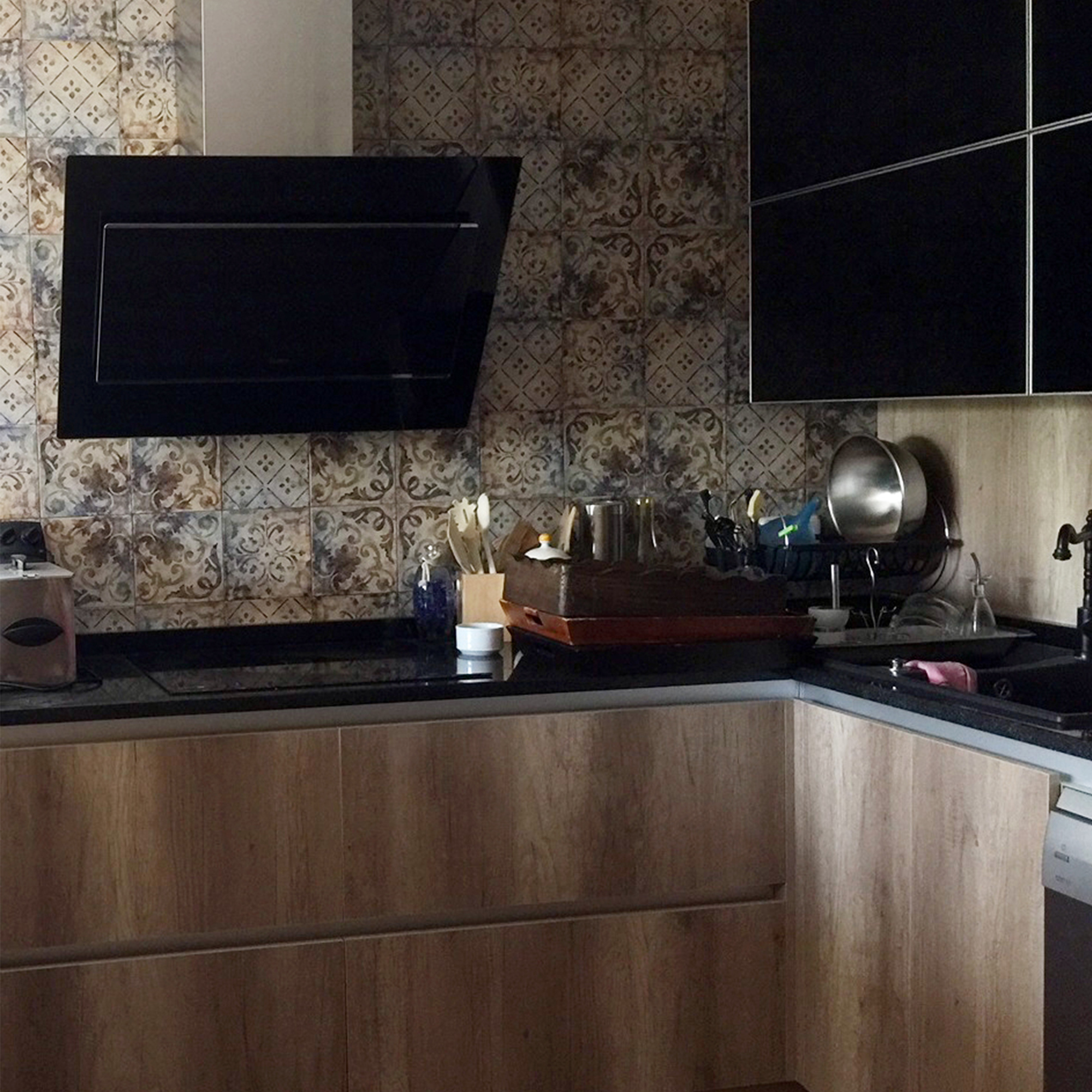 Cocina moderna con gabinetes de madera, azulejos estampados y campana extractora negra.
