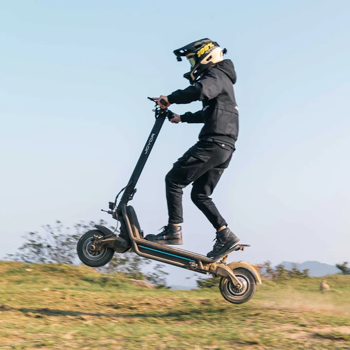 Un pilota con equipaggiamento protettivo esegue un salto con un monopattino elettrico in un campo.