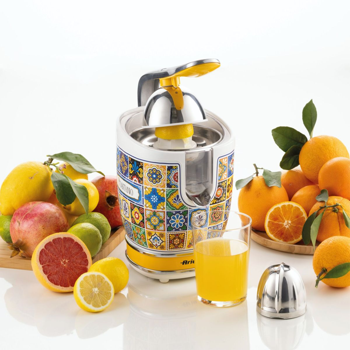 Exprimidor de cítricos estampado con vaso de jugo amarillo, limones frescos, naranjas y granadas sobre fondo blanco.