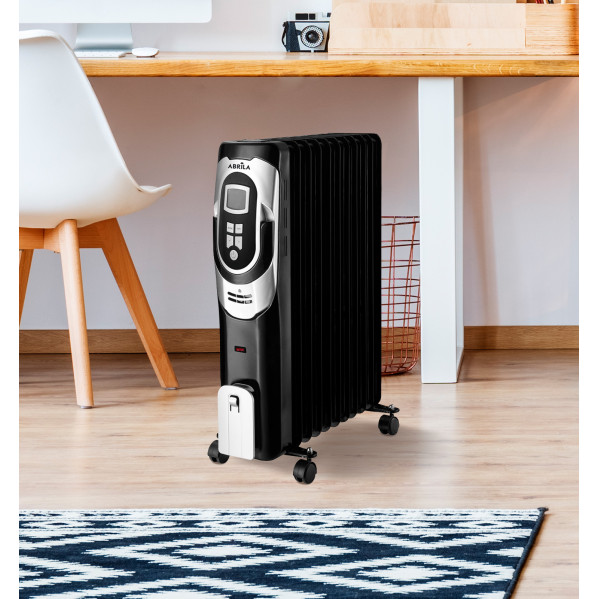 Un radiatore ad olio nero con comandi digitali su ruote in una stanza accanto a una sedia bianca e una scrivania in legno.