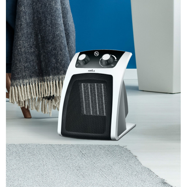 Un termoventilatore bianco con comandi neri si trova su un pavimento di legno davanti a una parete blu.
