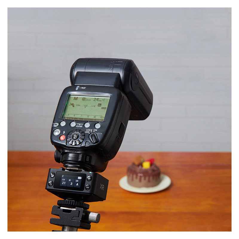 Un flash d'appareil photo avec écran LCD sur trépied, avec un petit gâteau au chocolat sur une table en bois en arrière-plan.