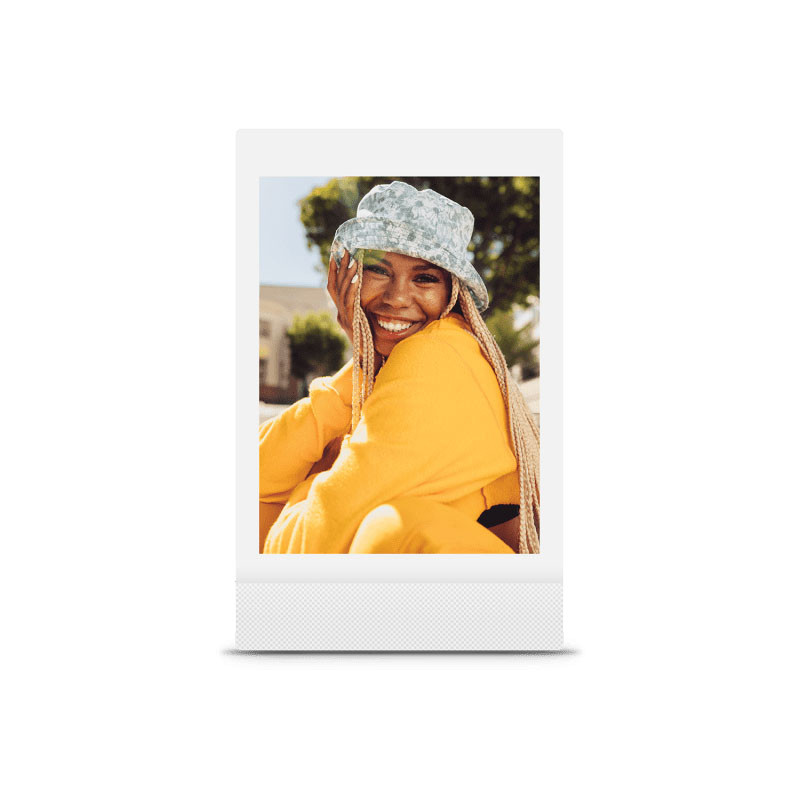 Una donna sorridente con cappello e maglione giallo su una foto Polaroid all'aperto.