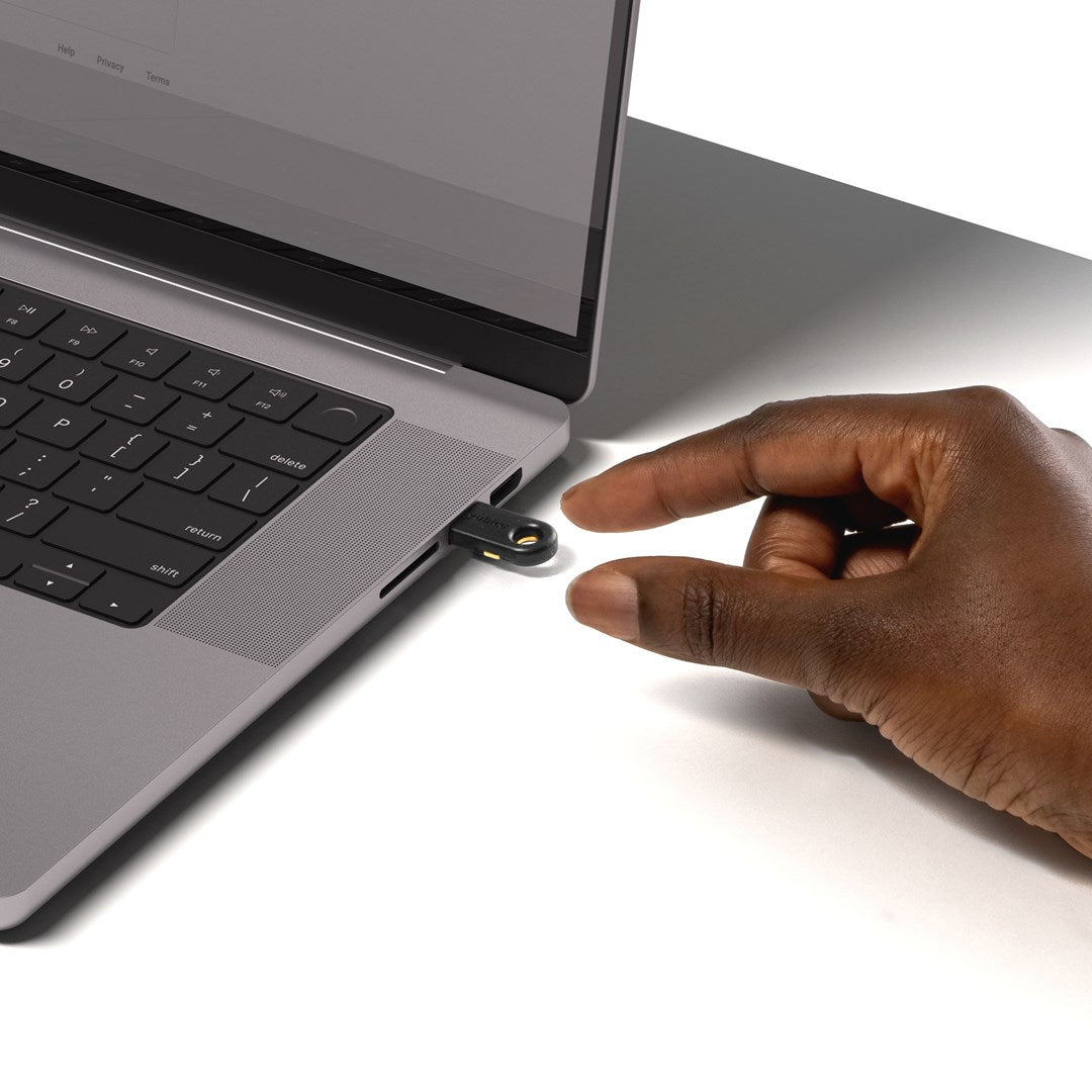 Eine Hand setzt einen schwarzen USB-Sicherheitsschlüssel in den Anschluss eines grauen Laptops ein.