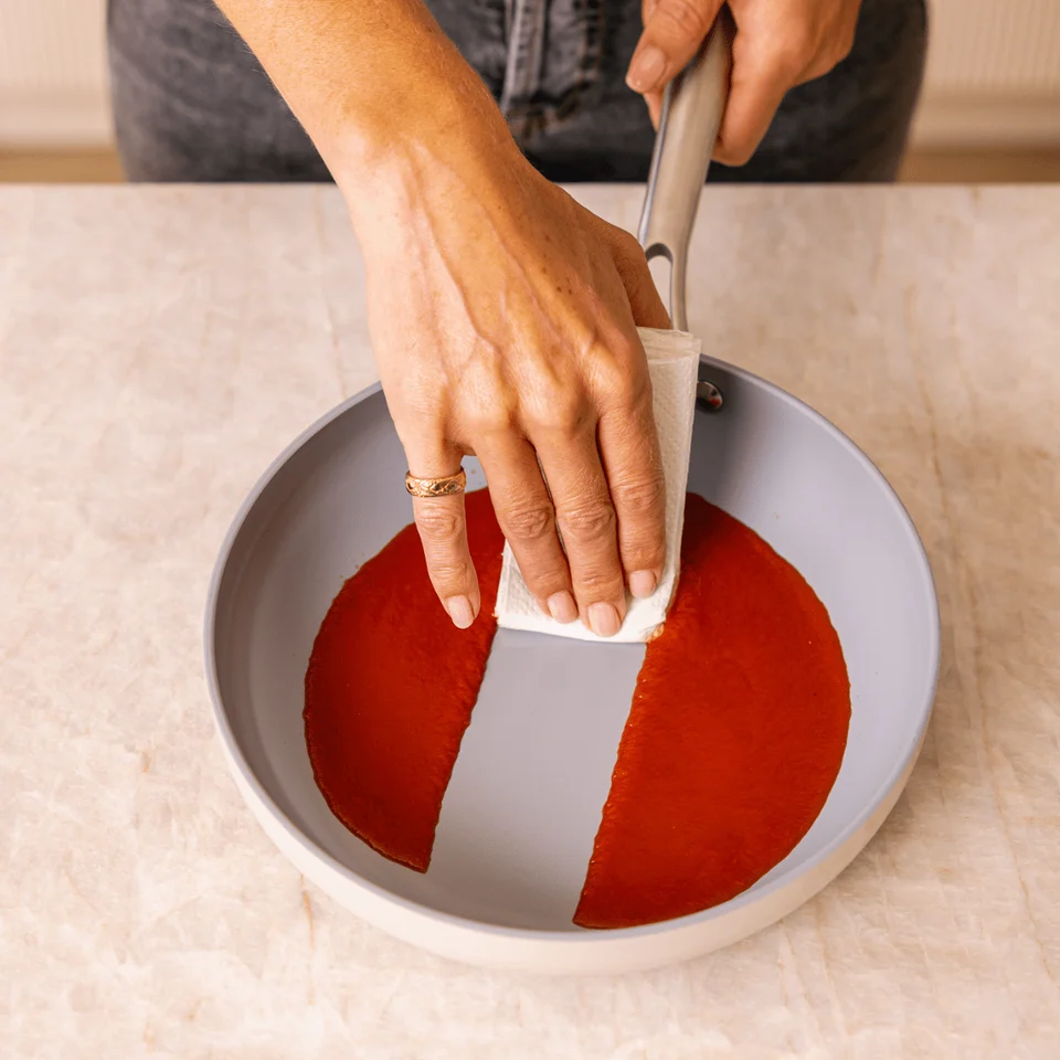 Someone is wiping sauce out of a pan with a paper towel.