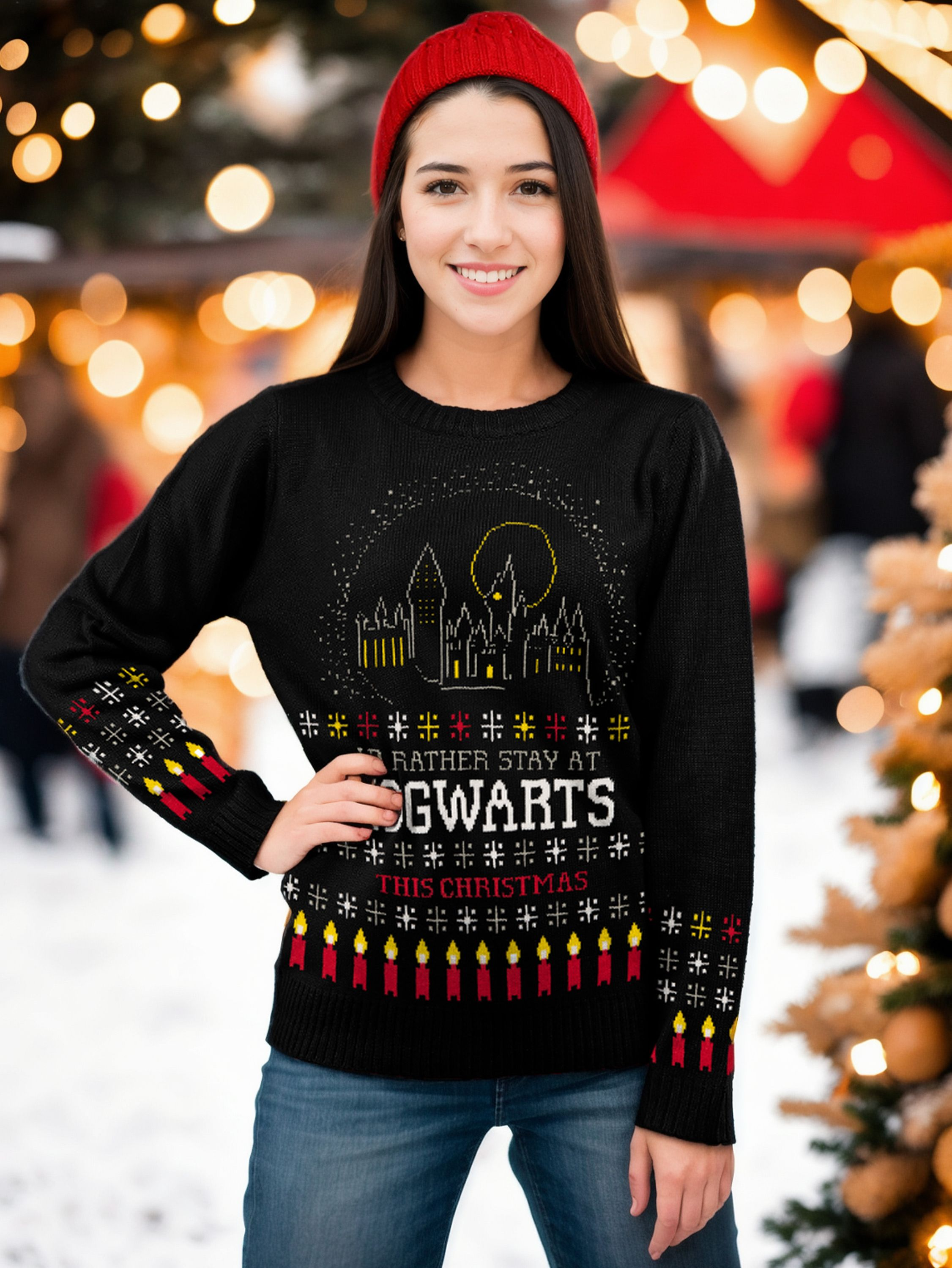 Eine lächelnde Frau mit roter Mütze und einem Hogwarts-Weihnachtspullover steht im Schnee vor Lichtern.