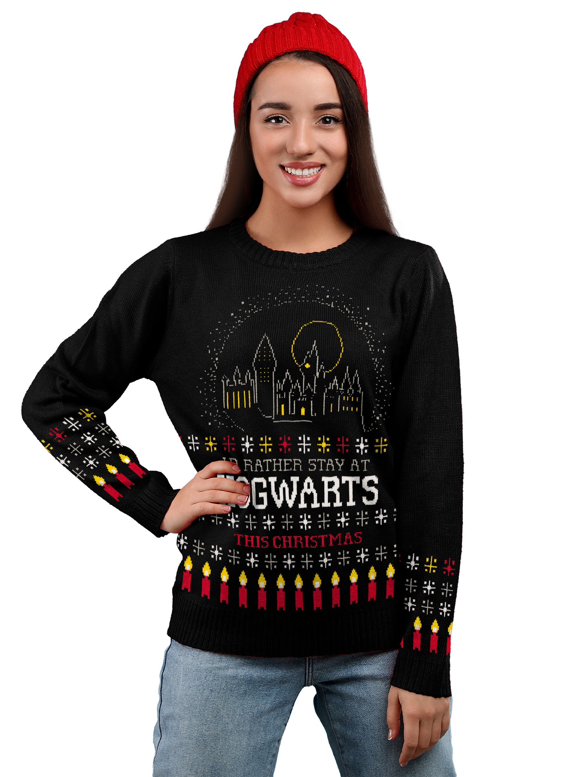 Eine lächelnde Frau mit roter Mütze und schwarzem Hogwarts-Weihnachtspullover mit Kerzen- und Schlossmotiven.