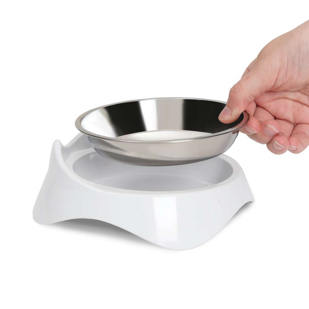 Una mano levanta un plato de acero inoxidable para mascotas de un soporte blanco de plástico.