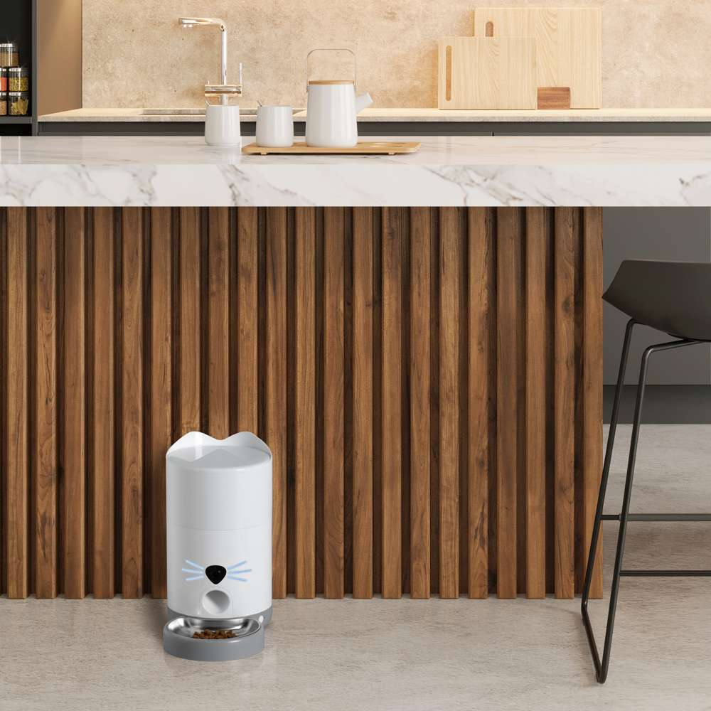 Un comedero automático blanco con temática de gato sobre el suelo de la cocina.