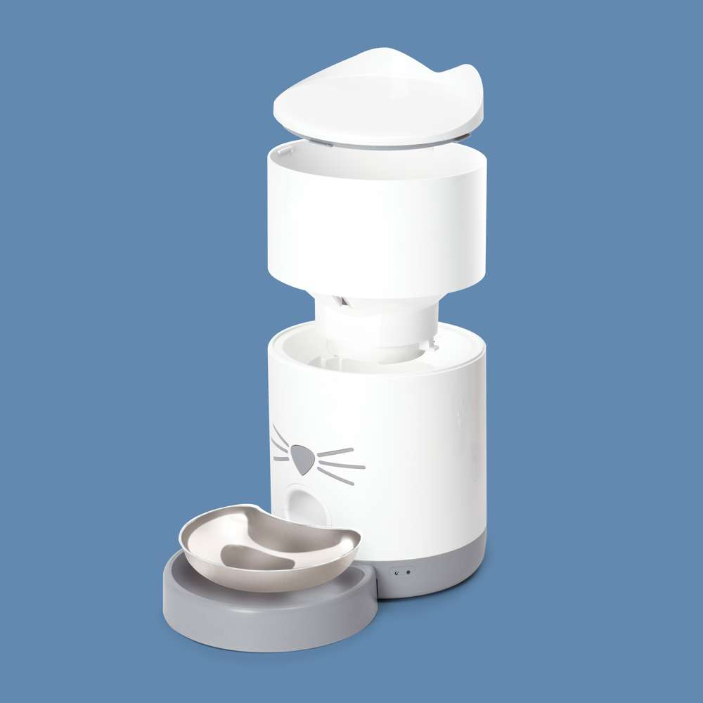 Un comedero automático blanco para mascotas con base gris y tapa con orejas de gato sobre fondo azul.