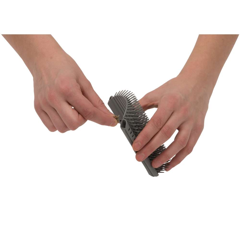 Manos sostienen un cepillo gris y curvado, quitando pelos de las cerdas.
