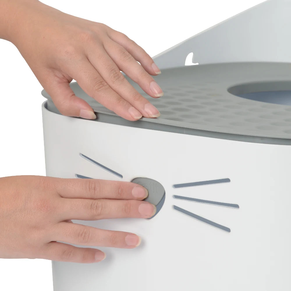 Manos tocando una caja de arena para gatos blanca con detalles grises.