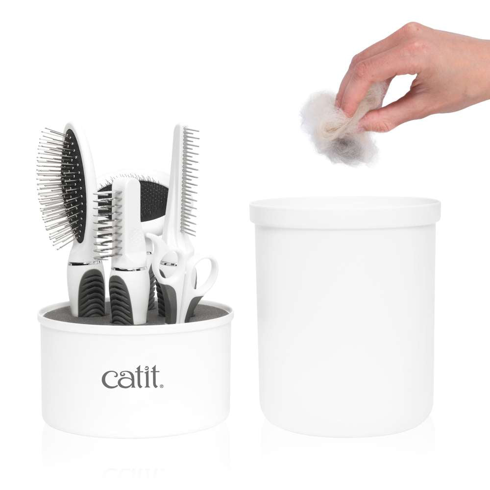 Una mano tira pelo de gato en un pequeño recipiente blanco junto a un soporte de aseo Catit.