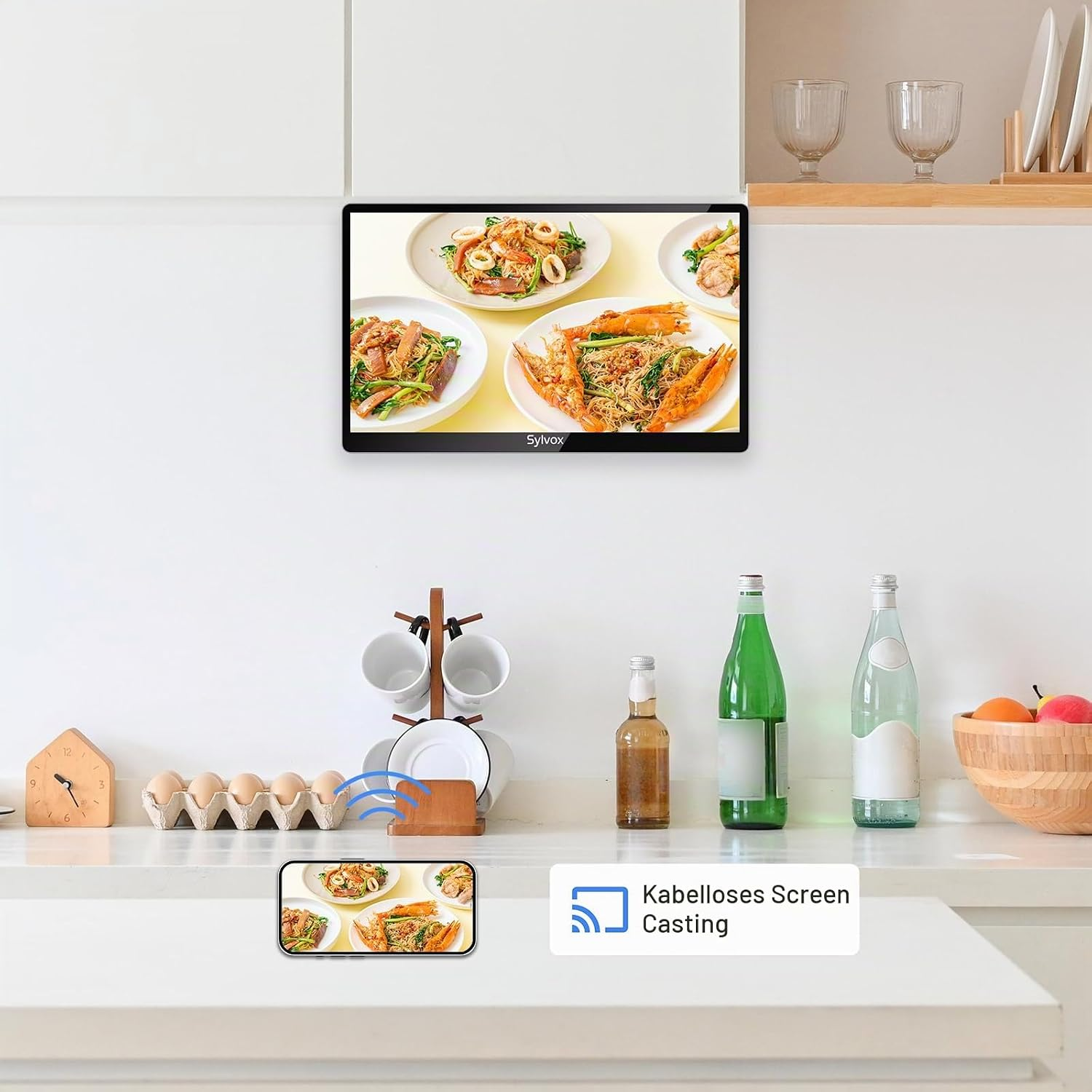 Una pantalla transmite de forma inalámbrica un video de cocina desde un teléfono en una cocina con botellas y fruta.