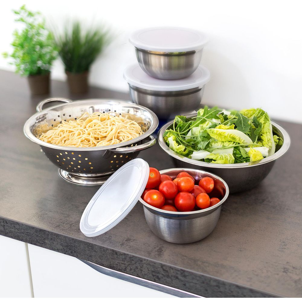 Edahlschüsseln und Sieb auf einer Küchentheke mit Spaghetti, Tomaten, Salat und Pflanzen im Hintergrund.