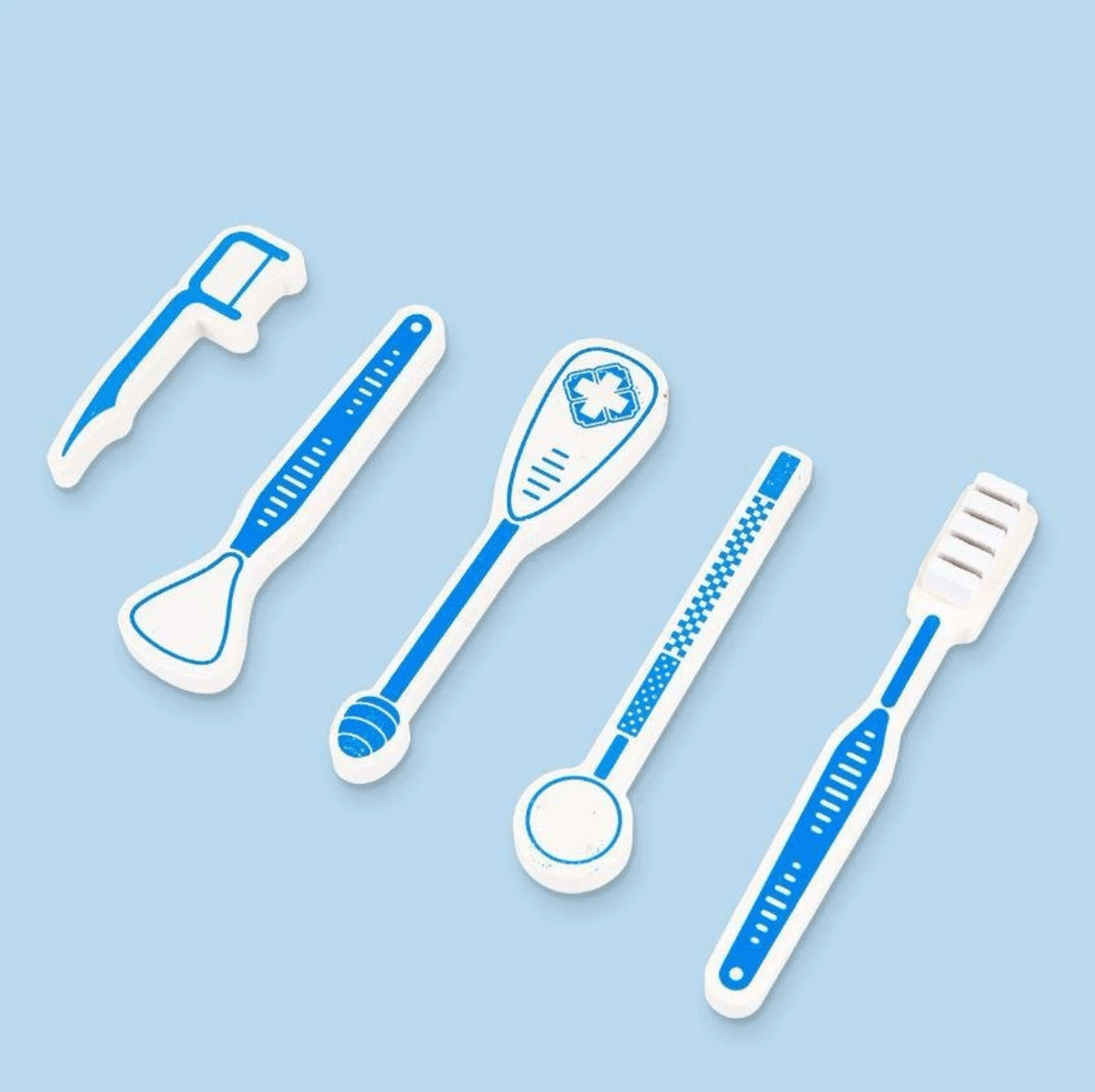 Cinco borradores dentales blancos y azules con forma de instrumentos de cuidado dental sobre un fondo azul claro.