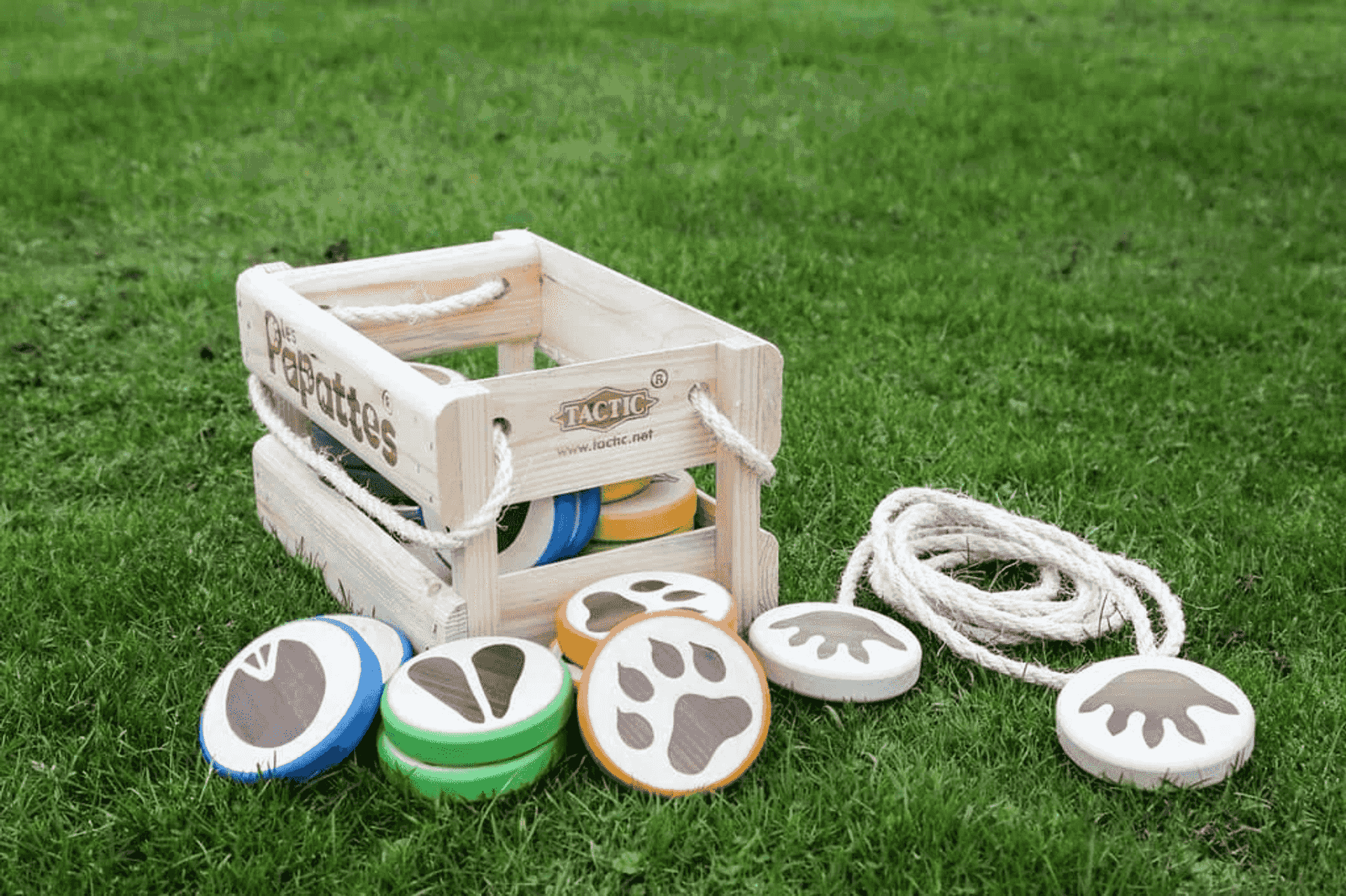 Una caja de madera con discos de huellas de animales y una cuerda sobre césped verde.