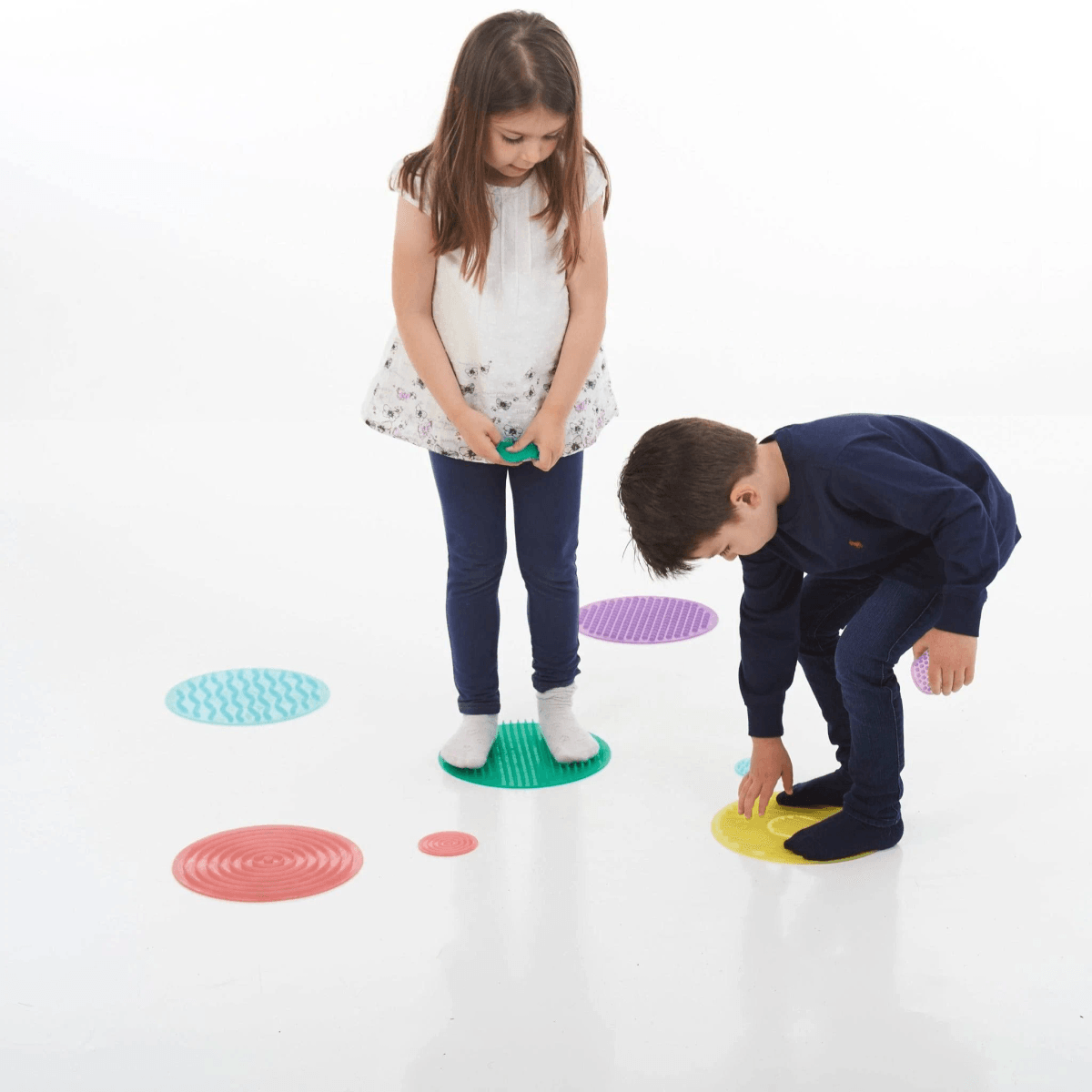 Dos niños juegan en el suelo blanco con círculos de silicona texturizados de colores.