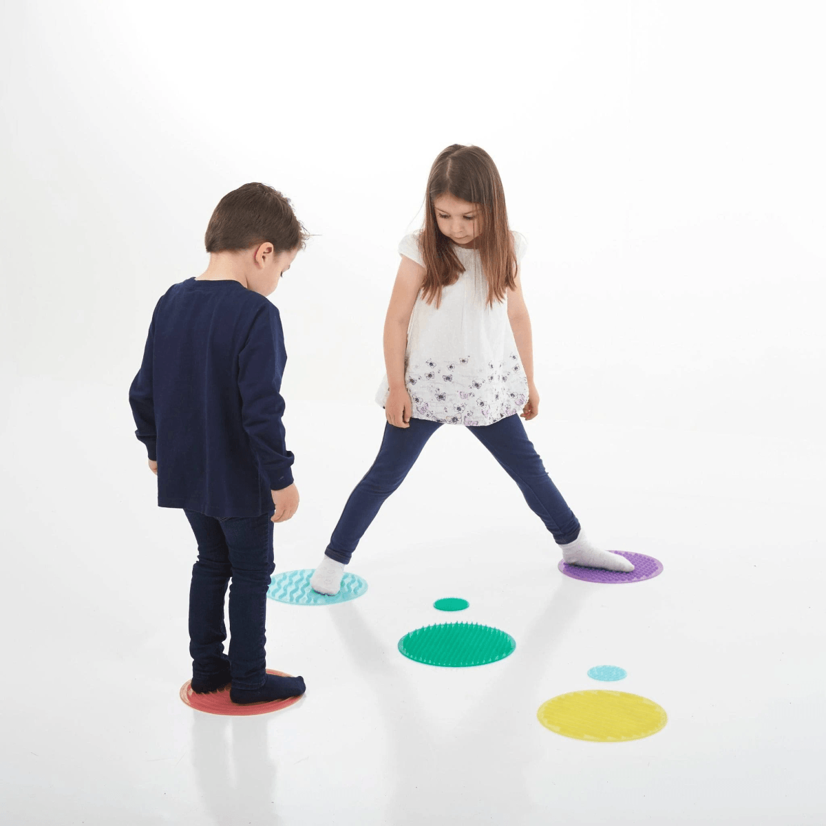 Dos niños se equilibran en discos texturizados coloridos sobre un fondo blanco.