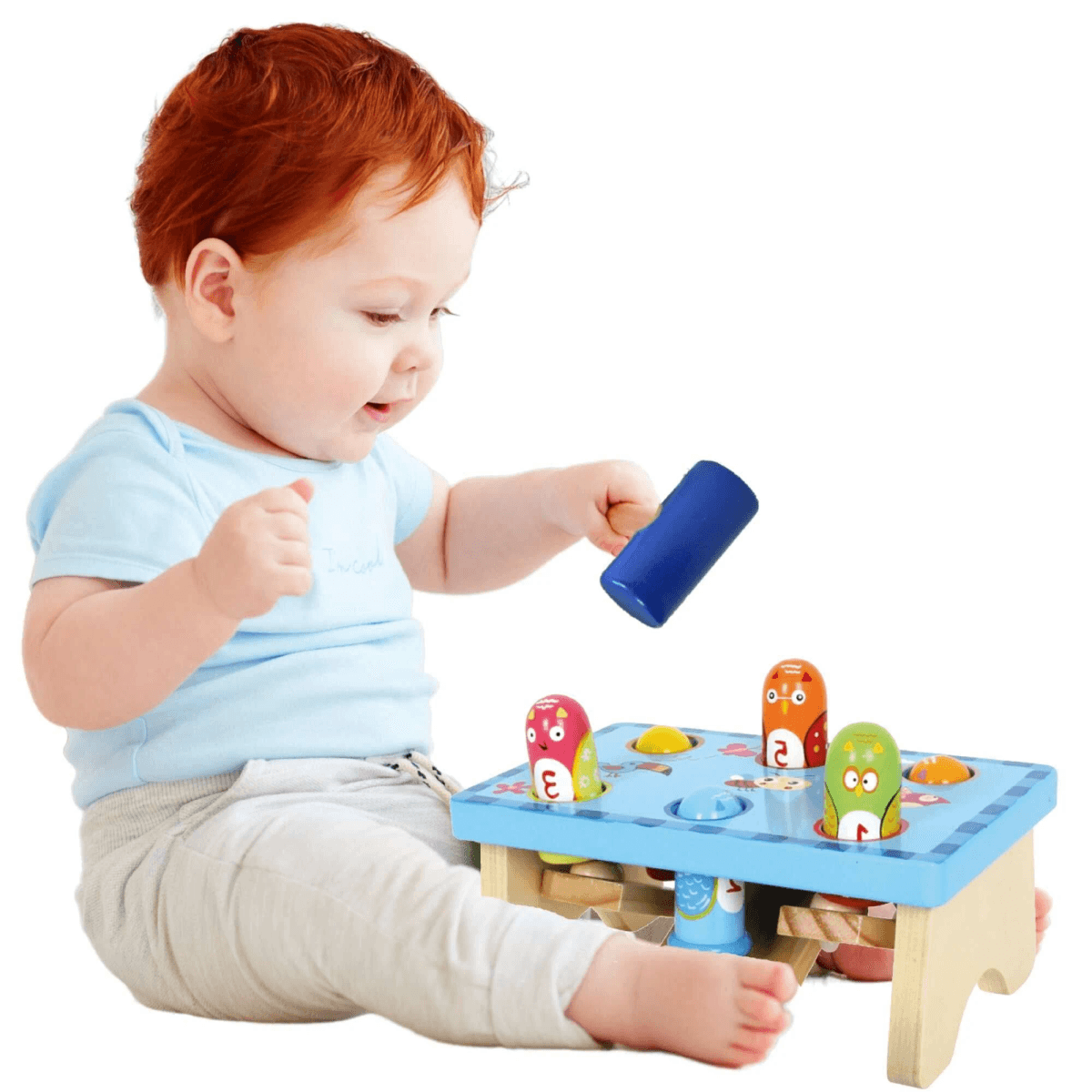 Un niño pelirrojo juega con un juguete de golpear azul sobre fondo blanco.