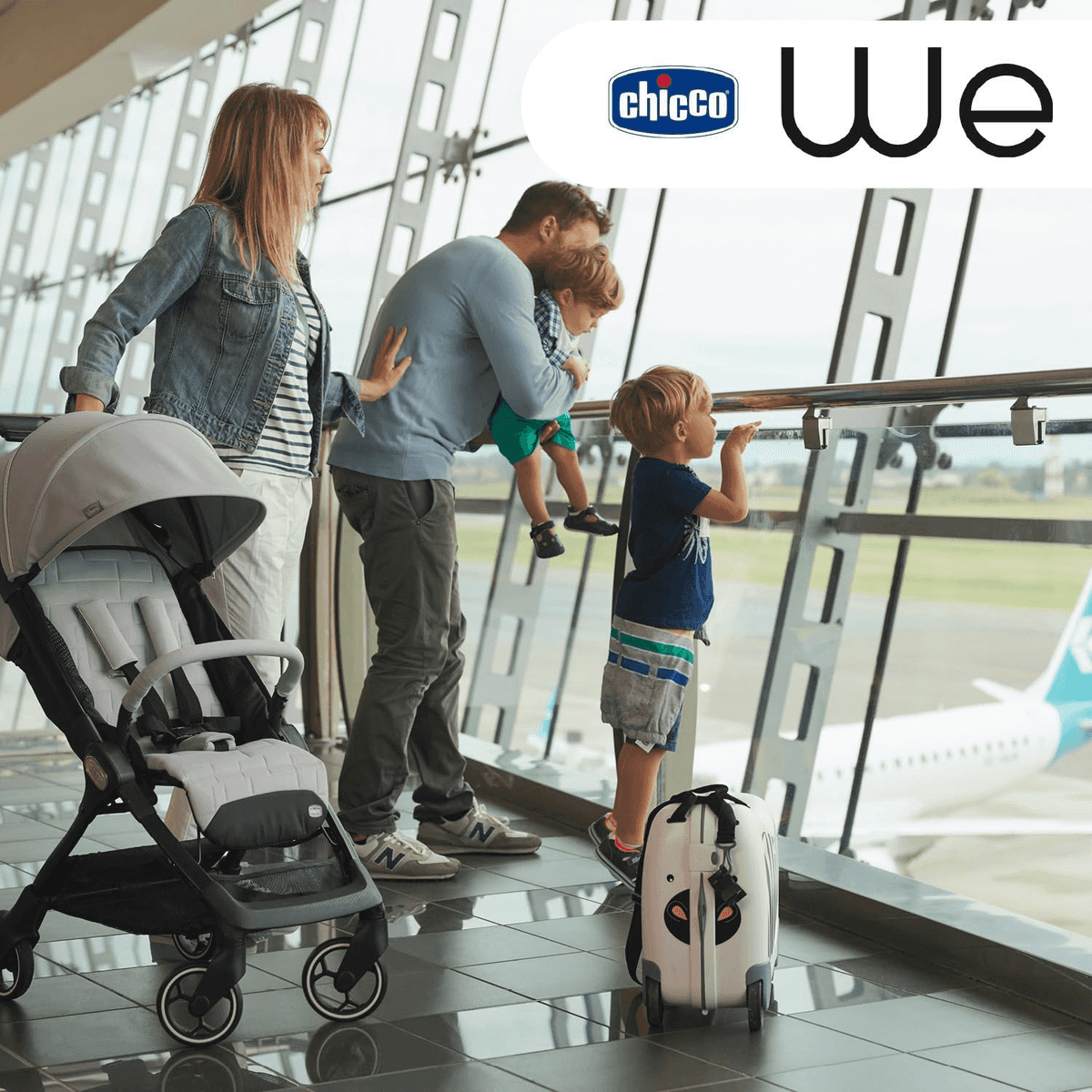 Una familia con dos niños y un carrito mira un avión a través de los ventanales del aeropuerto.