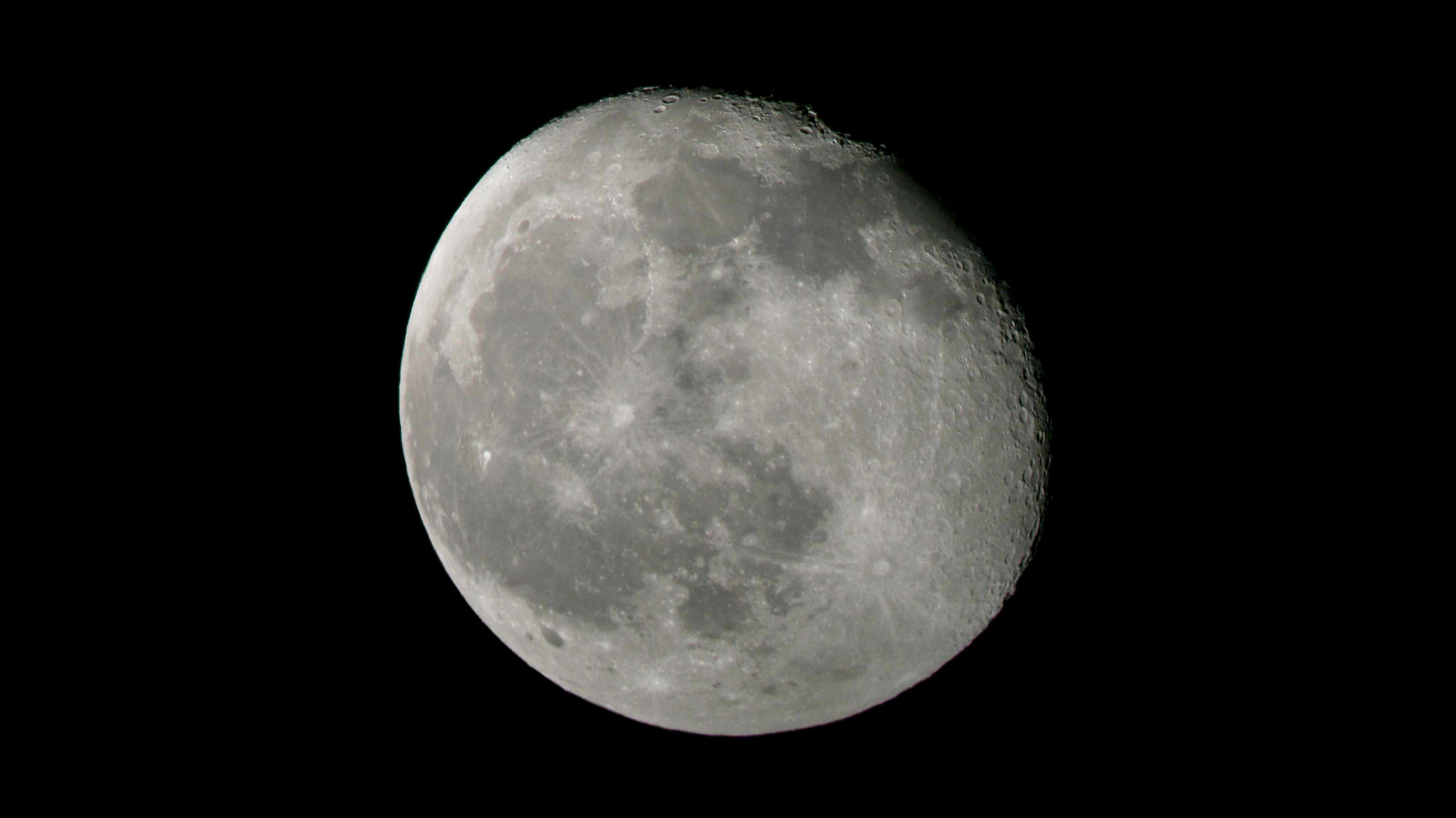 Vista detallada de la luna gibosa iluminada contra un cielo nocturno negro, mostrando cráteres y texturas.