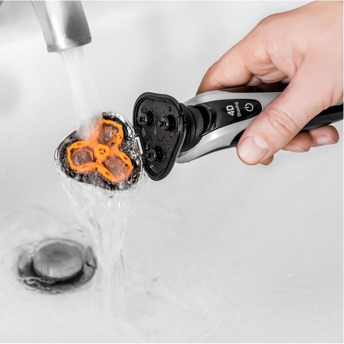 Una mano lava la testina rimossa di un rasoio elettrico sotto l'acqua corrente in un lavandino.