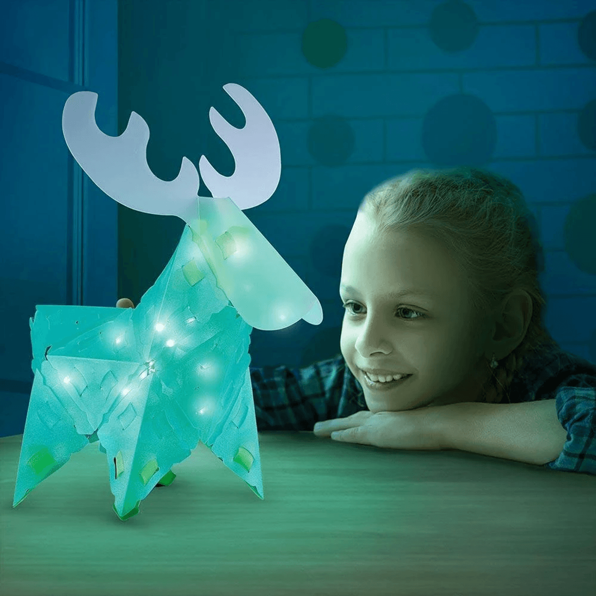 Una niña sonriente mira un reno de papel brillante en una habitación azul.