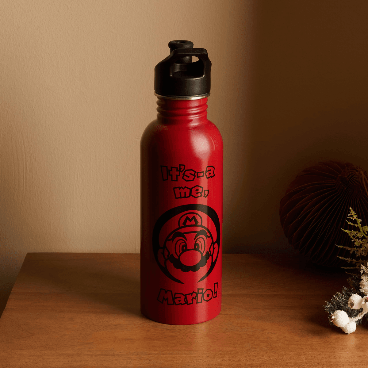 Una botella de agua roja de Mario se alza en una mesa de madera.