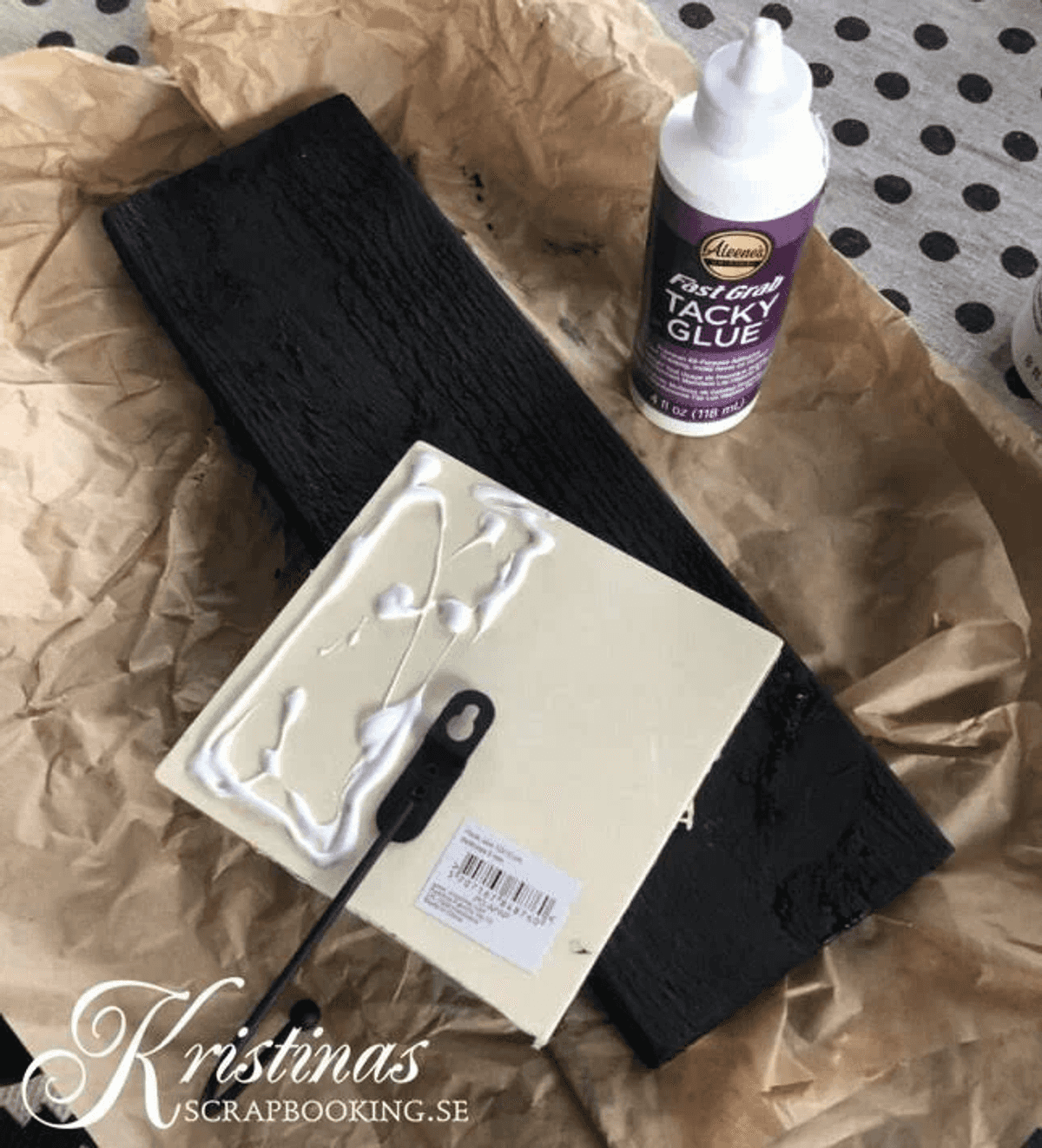 Manualidades sobre papel marrón con madera negra, pegamento blanco y un gancho.