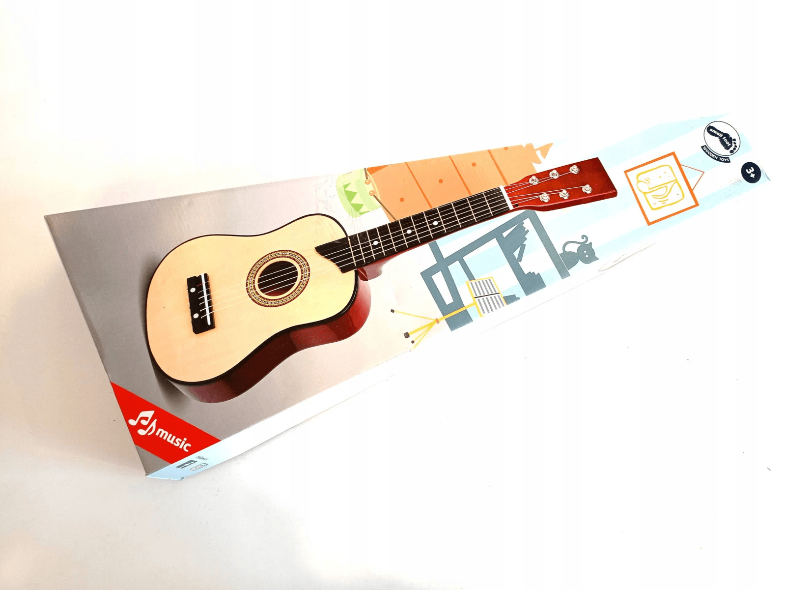 Una pequeña guitarra para niños yace diagonalmente en su embalaje impreso sobre fondo blanco.