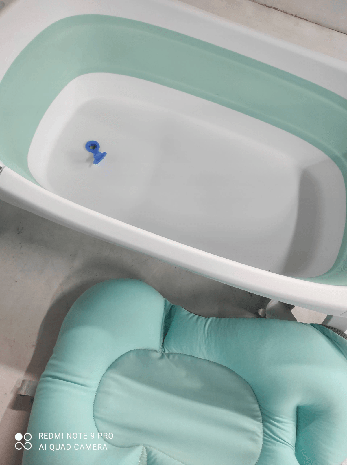 Una bañera para bebé plegable en verde menta y blanco con tapón azul y cojín a juego.