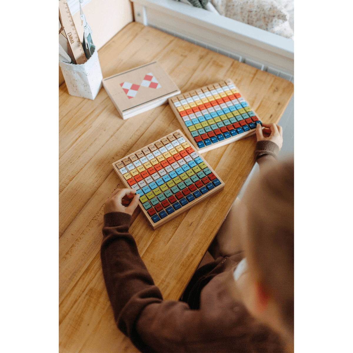 Un niño está sentado en una mesa de madera jugando con tableros de matemáticas.