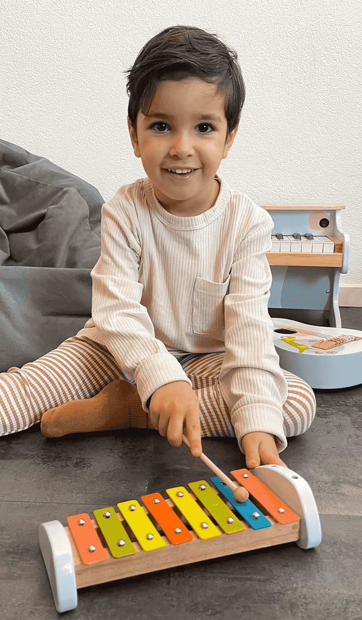 Un niño pequeño se sienta en el suelo, sonriendo mientras toca un xilófono colorido.