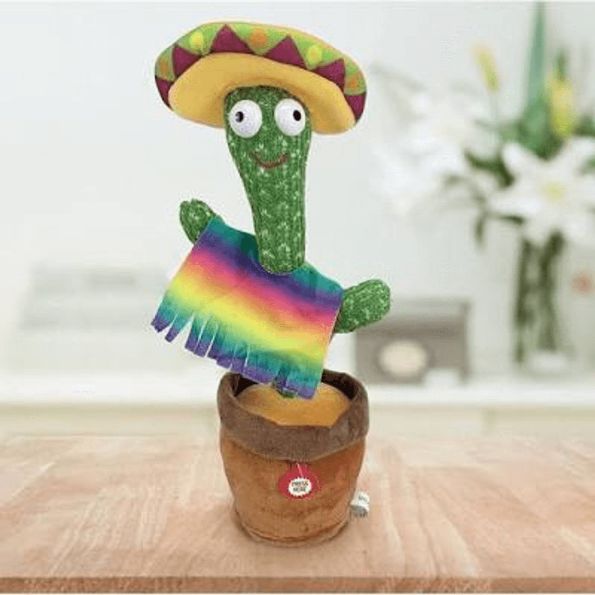 Un cactus de peluche verde con sombrero y un poncho colorido en una maceta marrón sobre una mesa de madera.