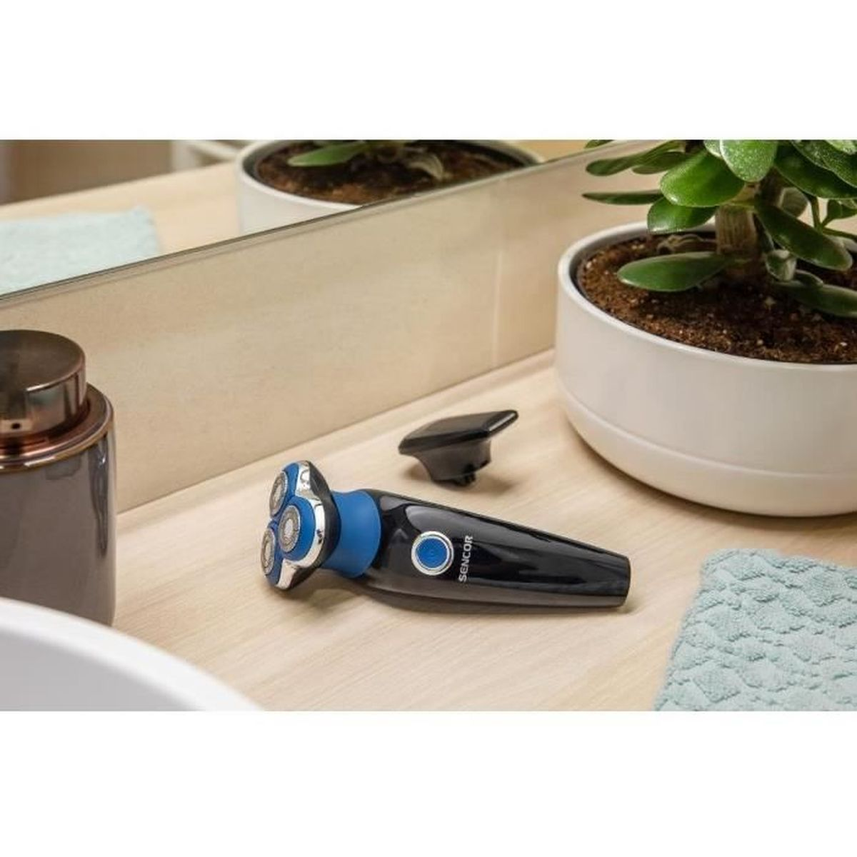 Un rasoio elettrico nero e blu si trova sul bancone del bagno vicino a una pianta in vaso e a un dispenser.