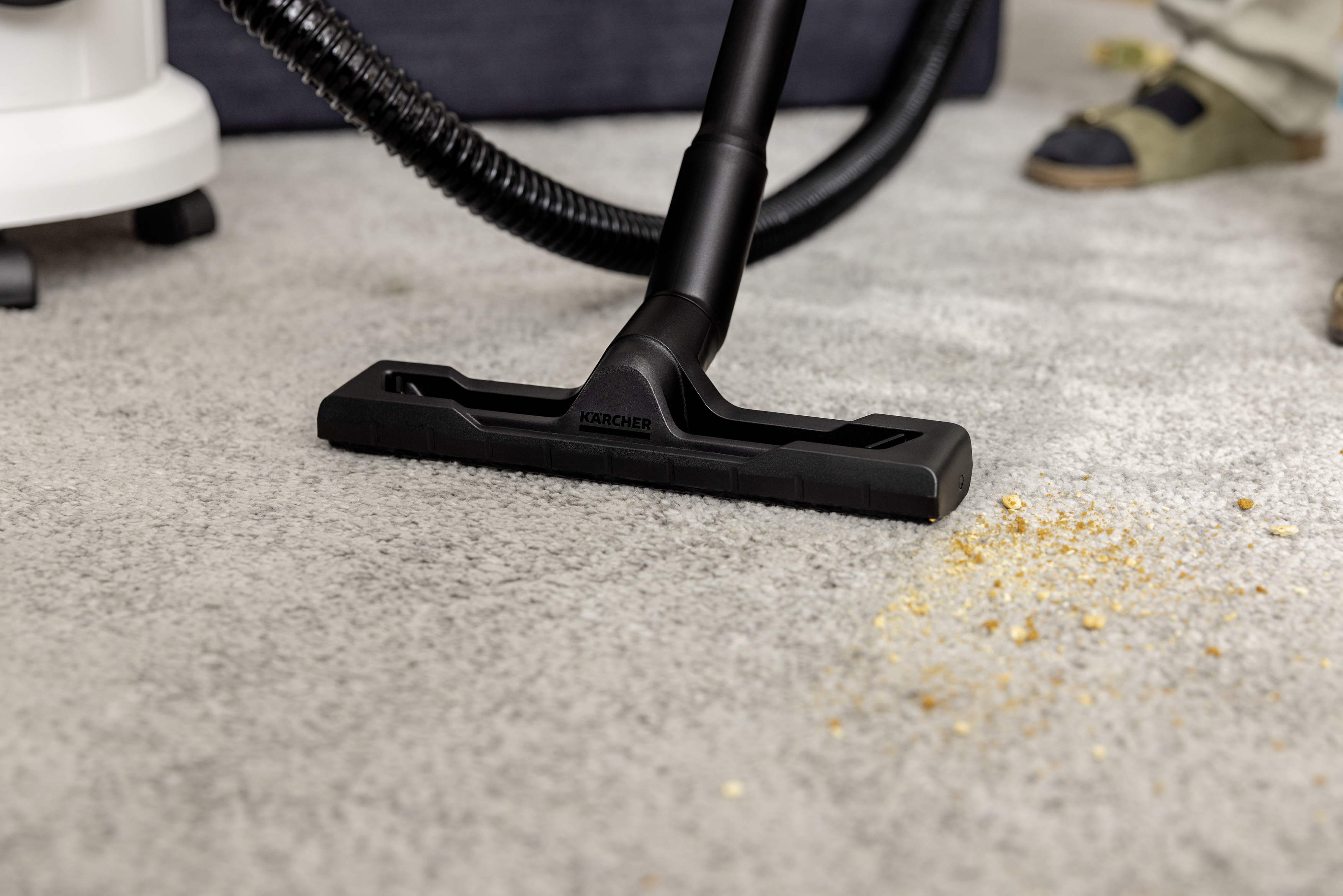 Una bocchetta per aspirapolvere Karcher nera su un tappeto grigio chiaro raccoglie briciole.