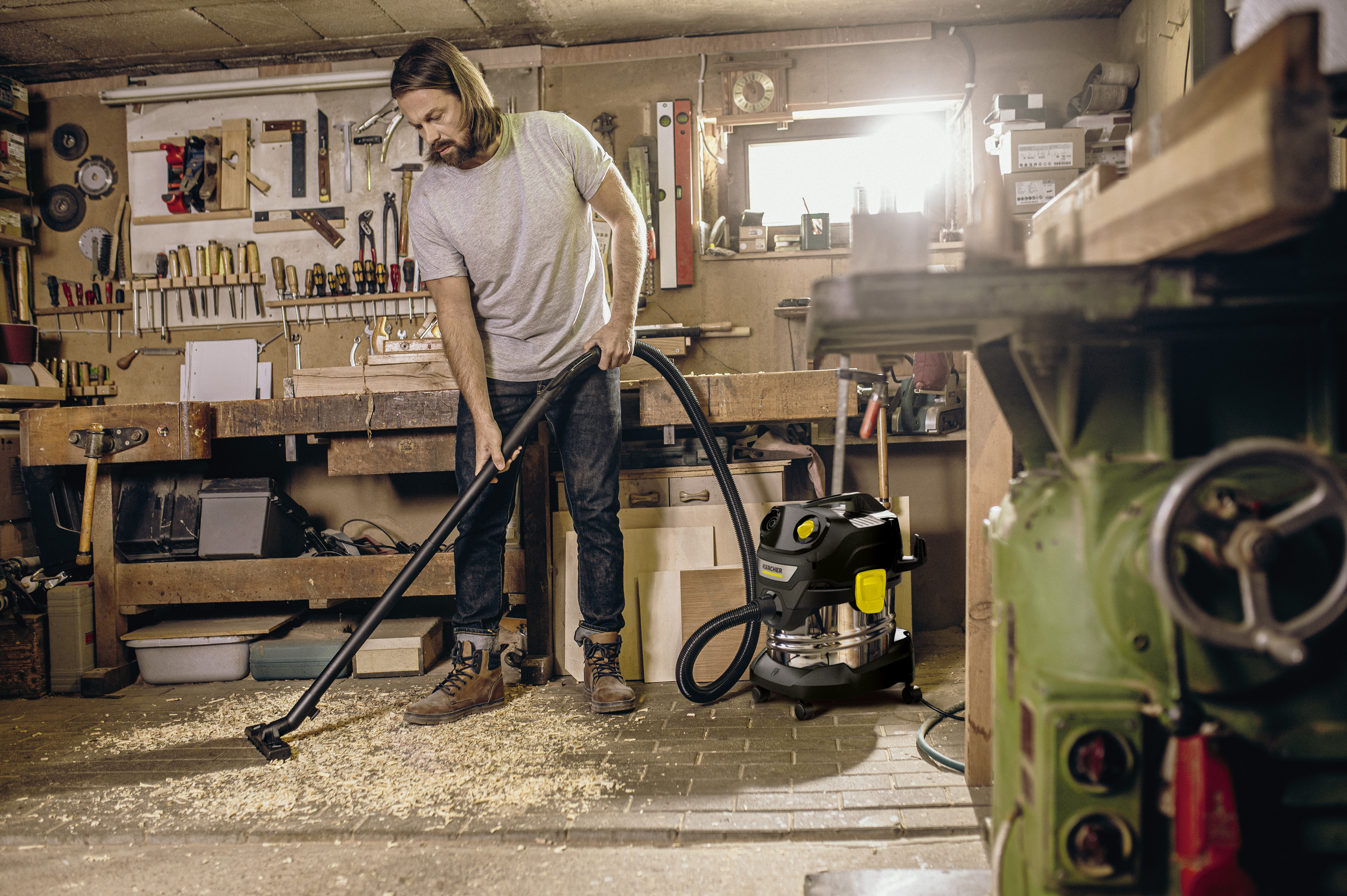 Un uomo aspira trucioli di legno in un'officina con un aspiratore nero e giallo.