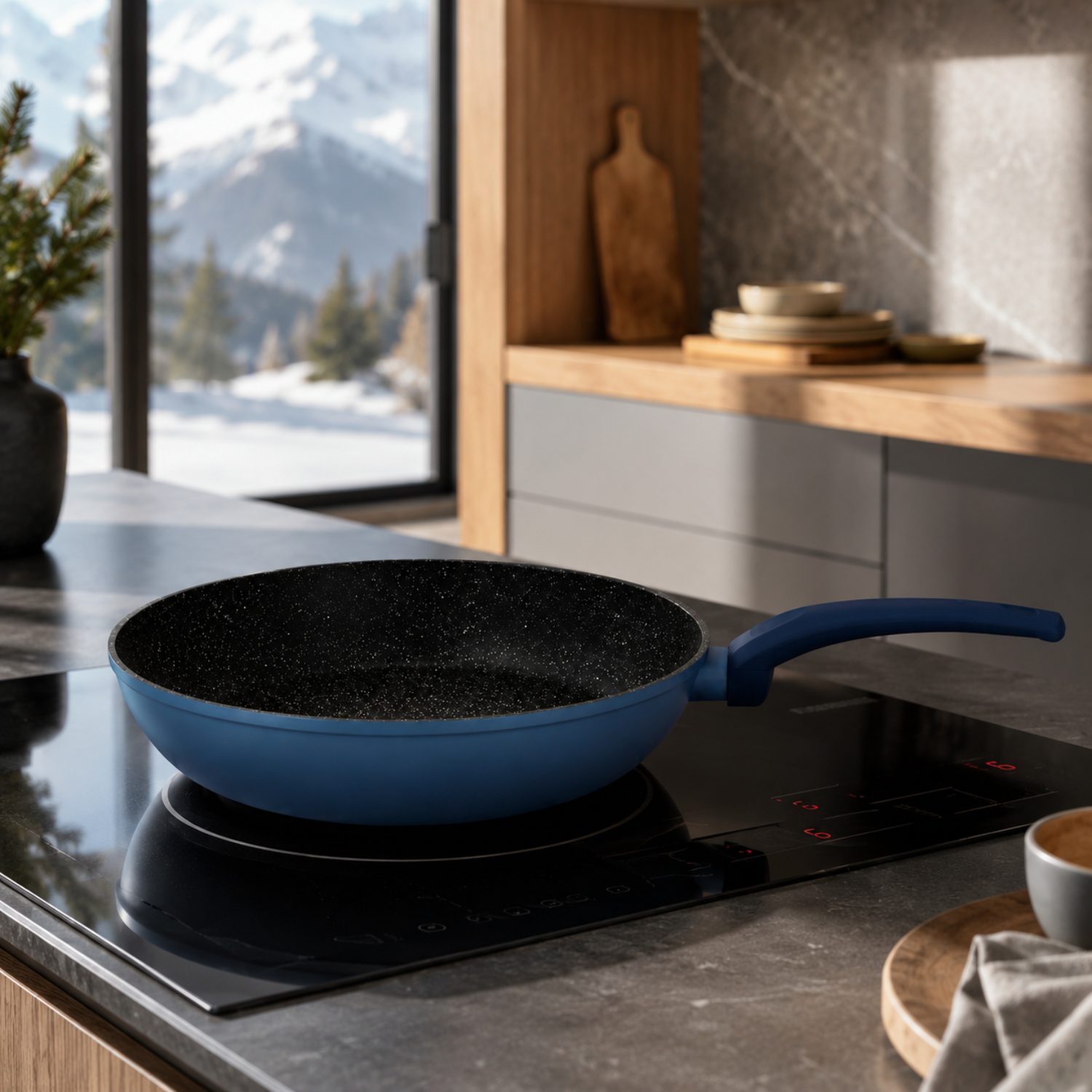 Padella blu su un piano cottura in una cucina moderna con vista sulle montagne innevate.
