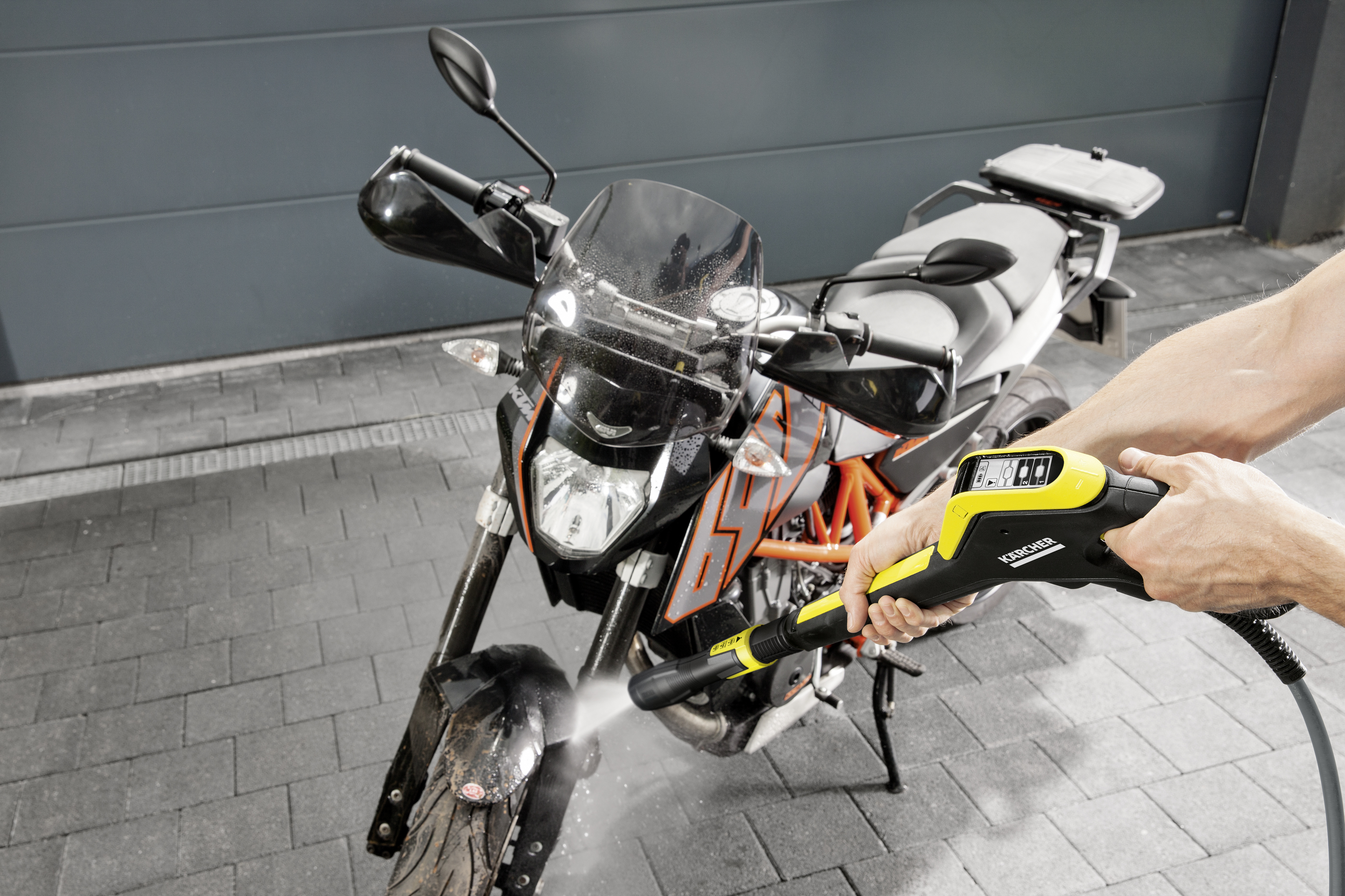Una persona pulisce una moto sporca con un idropulitrice Karcher gialla e nera.