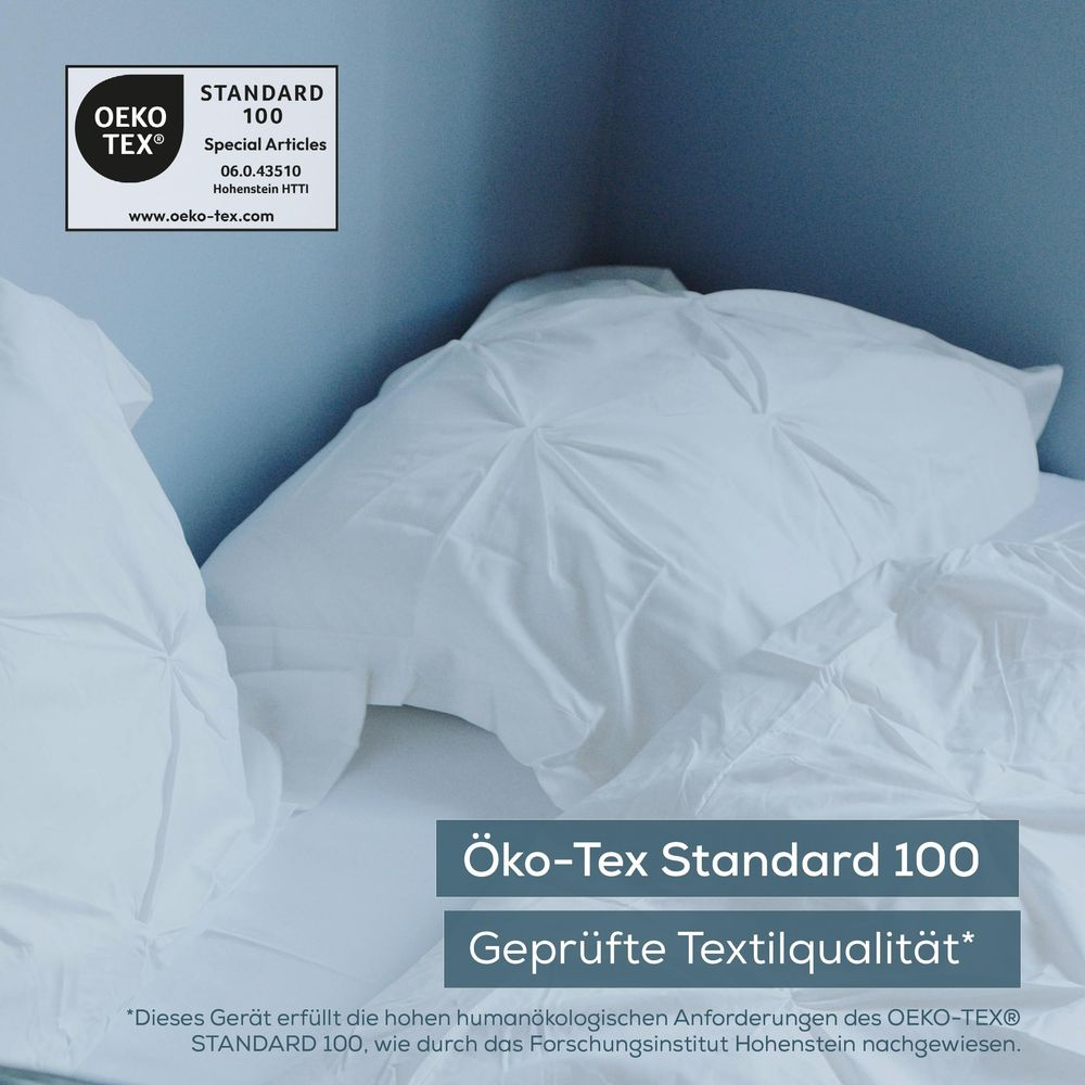 Weisse Kissen auf einem Bett vor blauer Wand mit Oeko-Tex-Zertifizierung.