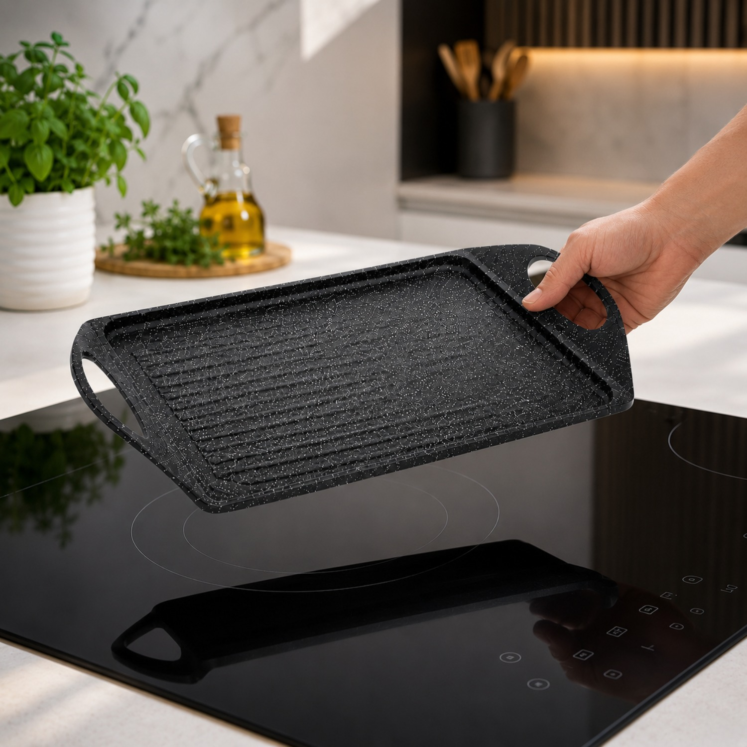 Una mano tiene una piastra nera sopra un piano cottura in vetroceramica in una cucina moderna.